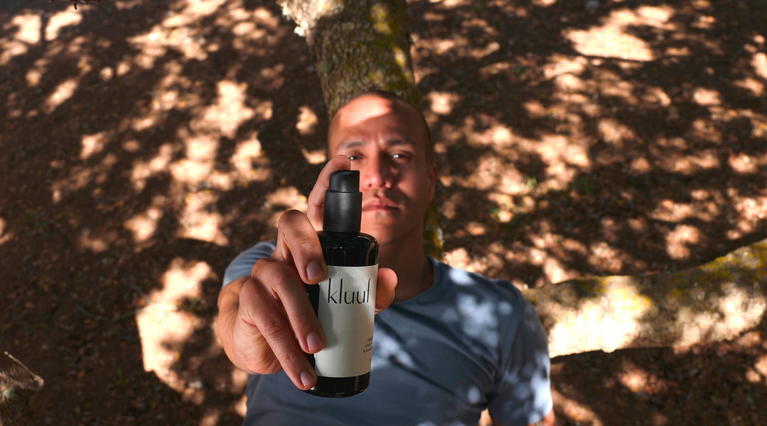 Male model lying in nature, holding Kluuf's gentle facial cleanser