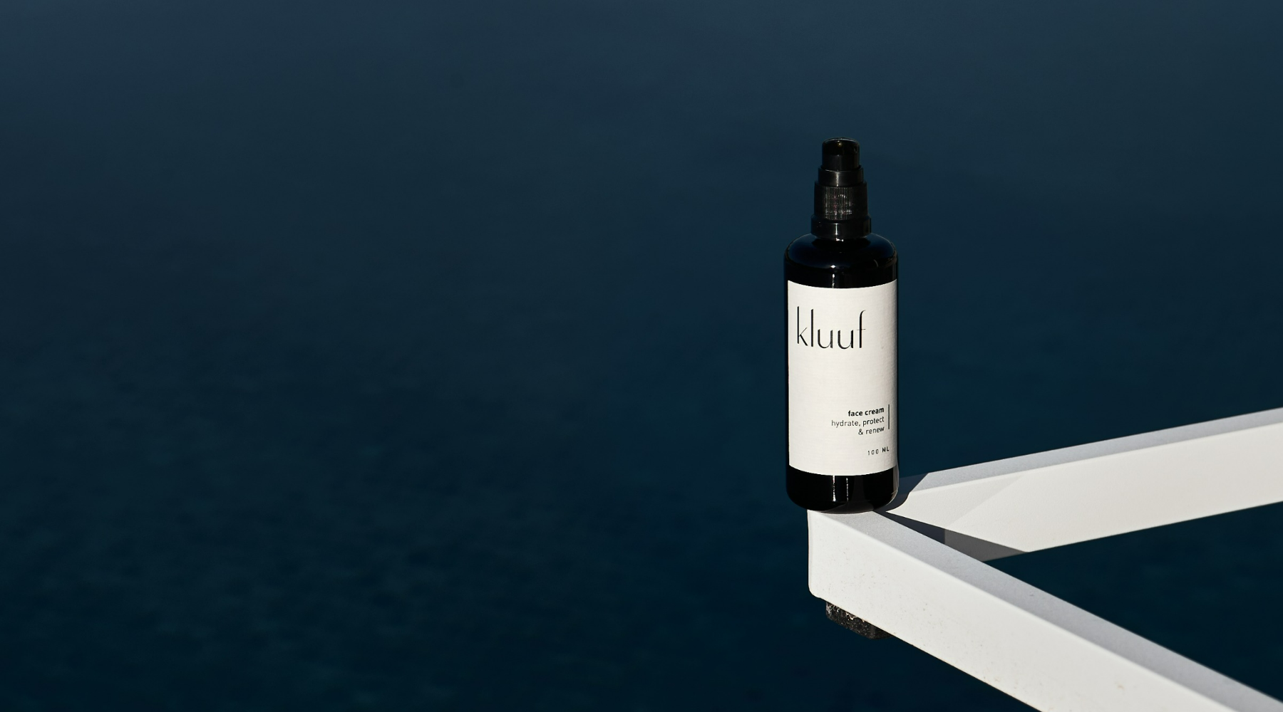 Bottle of Kluuf face cream in front of natural blue water