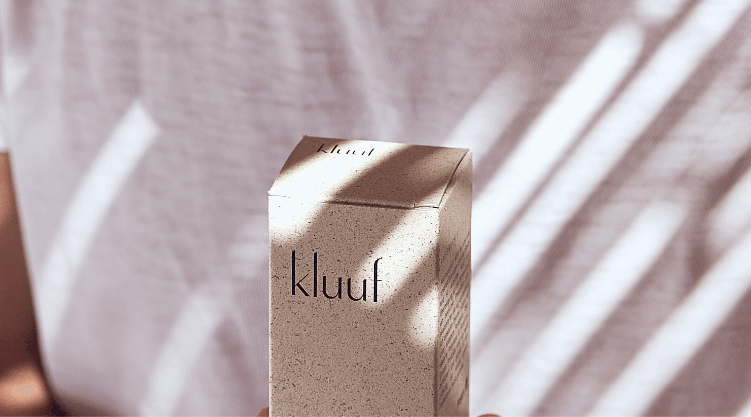 Close-up Kluuf face cream packaging in front of white t-shirt