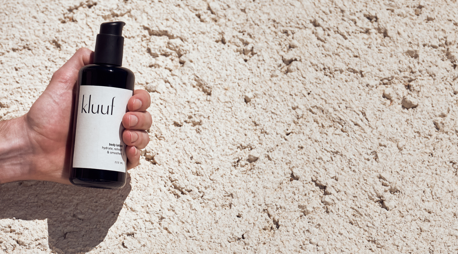 hand holding kluuf's vegan body lotion for men in front of bright stone wall