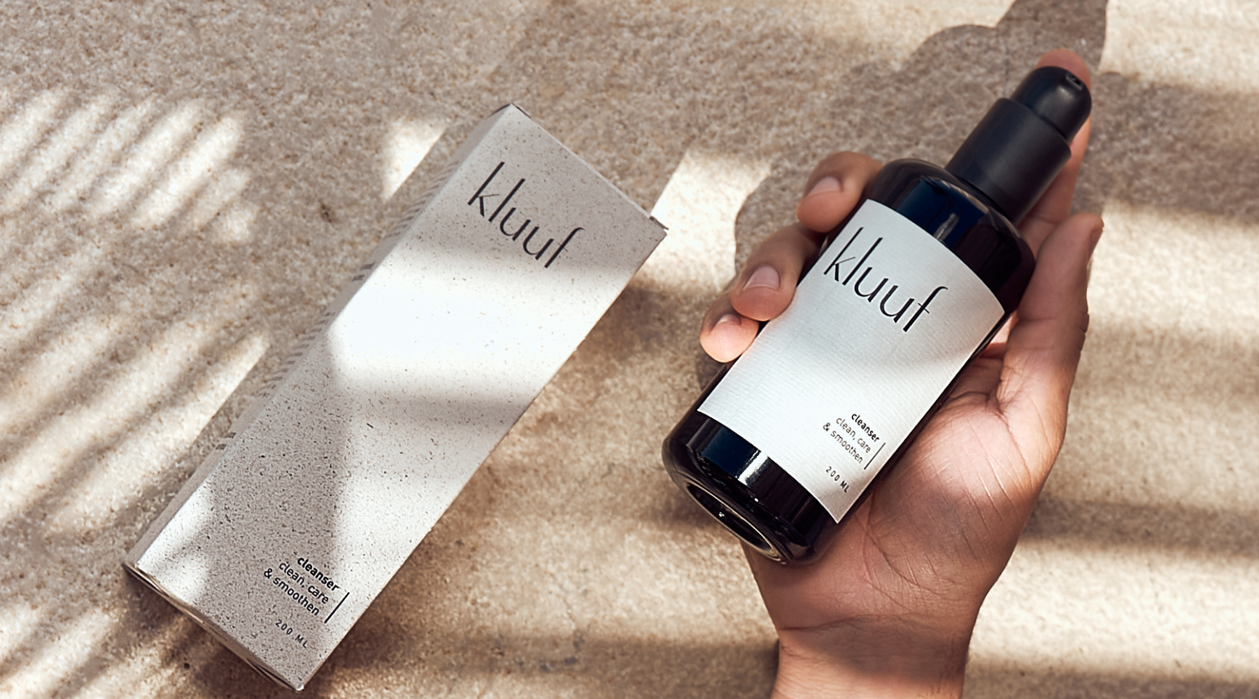 hand holding kluuf's gentle facial cleanser on ground with luxurious packaging and shadow